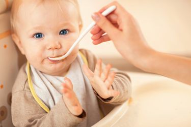 Ein Baby wird von der Mutter gefüttert und klatscht in die Hände