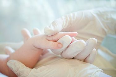 Arzthand mit Handschuh hält eine Kinderhand