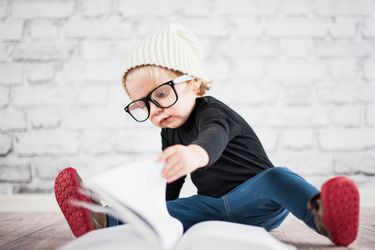 Junge mit cooler Brille und Haube blättert vor einer Ziegelmauer in einem Buch